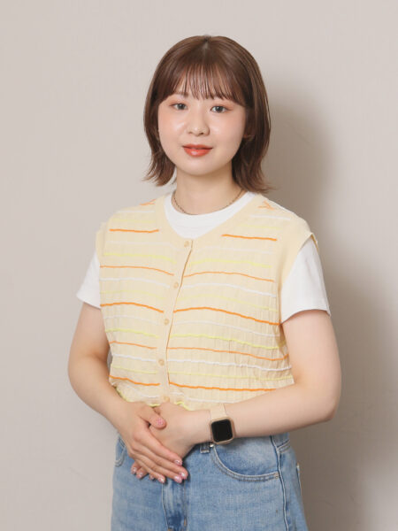 Portrait of a young woman with short brown hair, wearing a pale striped cardigan over a white tee and blue jeans, hands clasped in front.